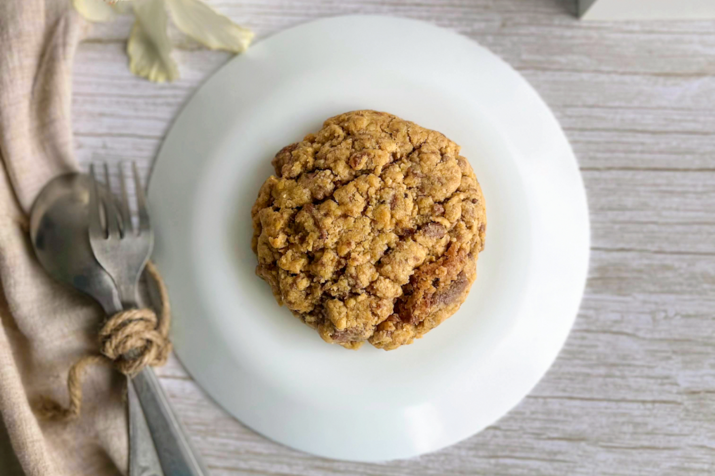 Cookie on a white plate with a fork and spoon on a wooden surface